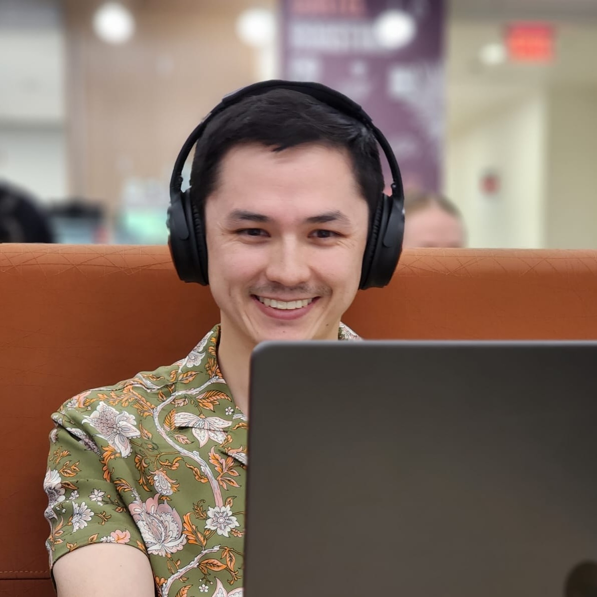 Hugh Berryman at his laptop, smiling and wearing headphones.